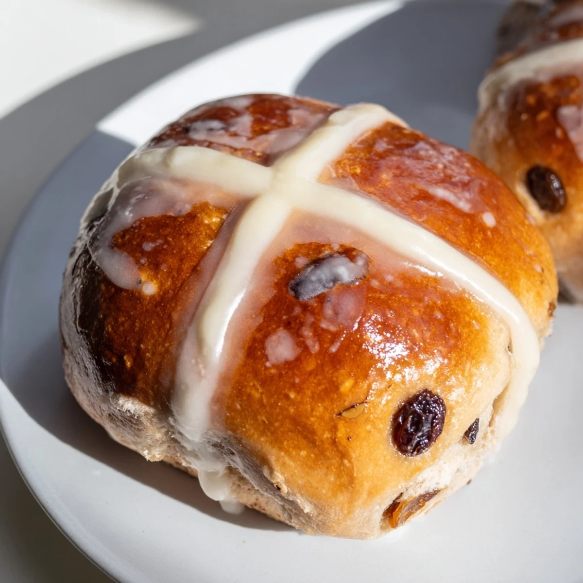 Warmly glazed Hot Cross Buns with currants and spices, fresh from the oven on a rustic wooden board.  