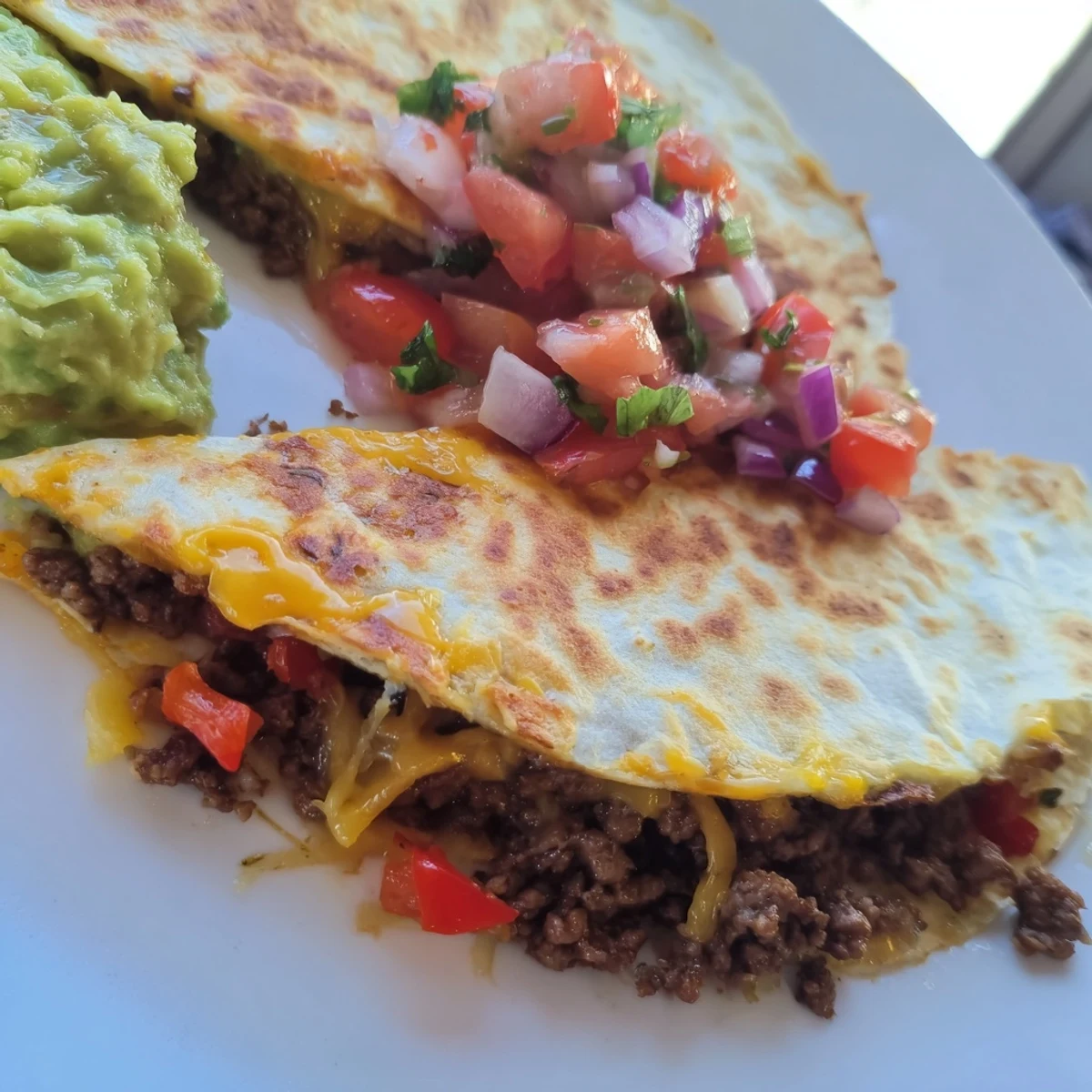 Sizzling skillet of freshly cooked Beef Quesadillas with Salsa and Guacamole served with sour cream on a rustic table.