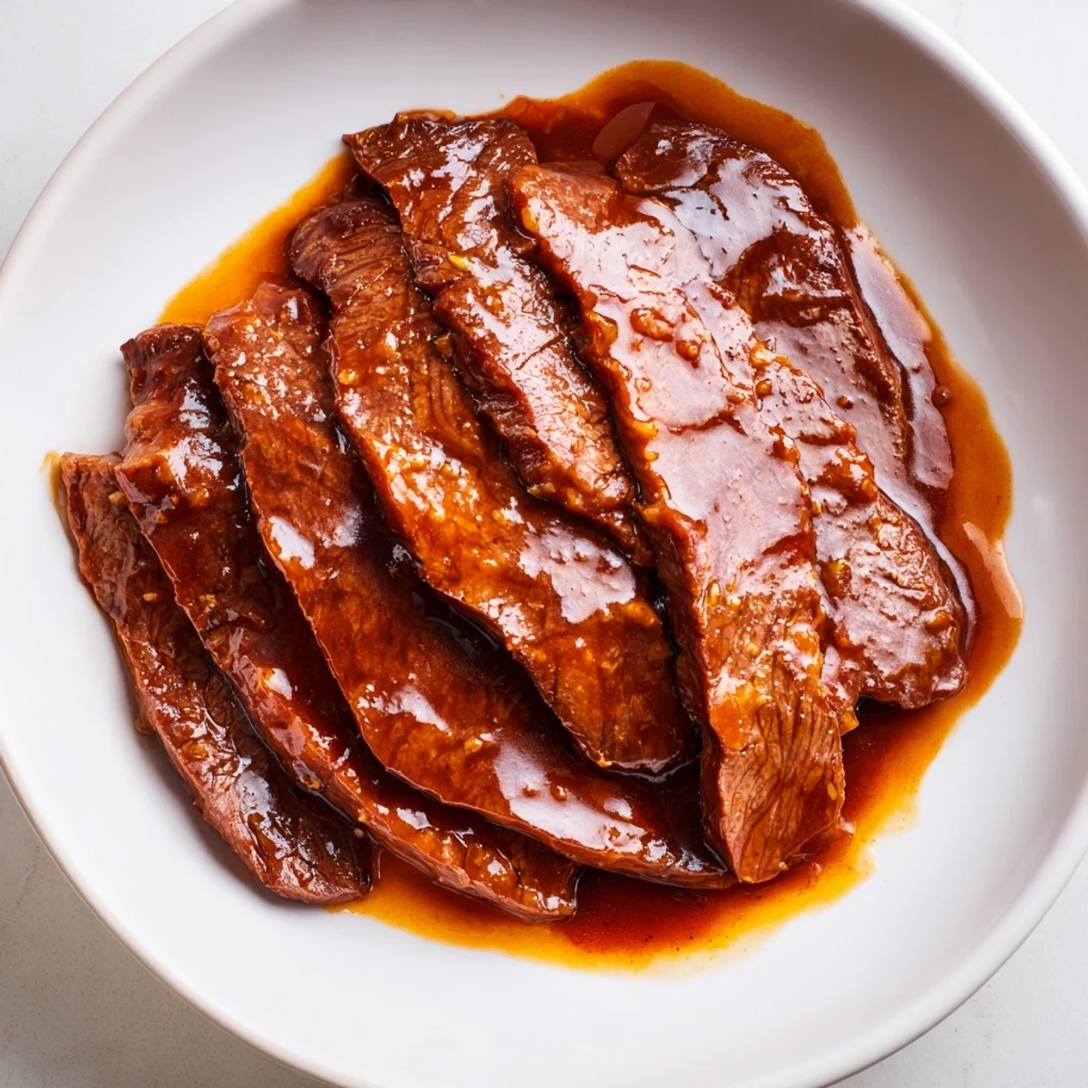 Ultimate Slow Cooker Mongolian Beef, tender and sweet, steams over white rice with green onions for garnish.
