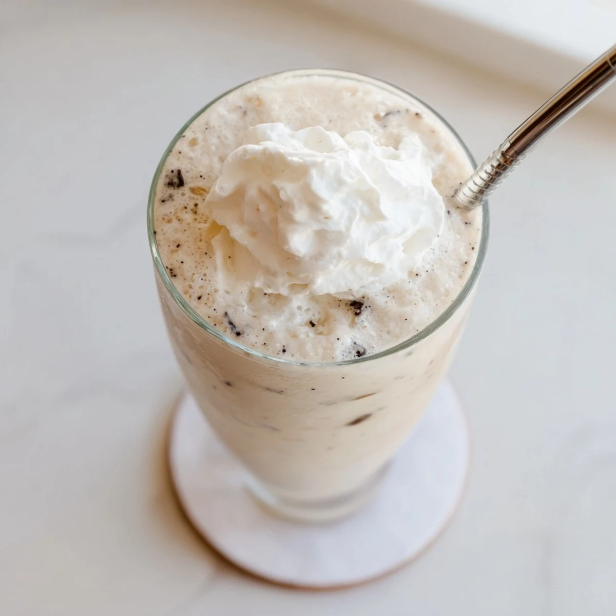 A tall glass of Vanilla Bean Frappuccino topped with whipped cream and a vanilla bean pod.  