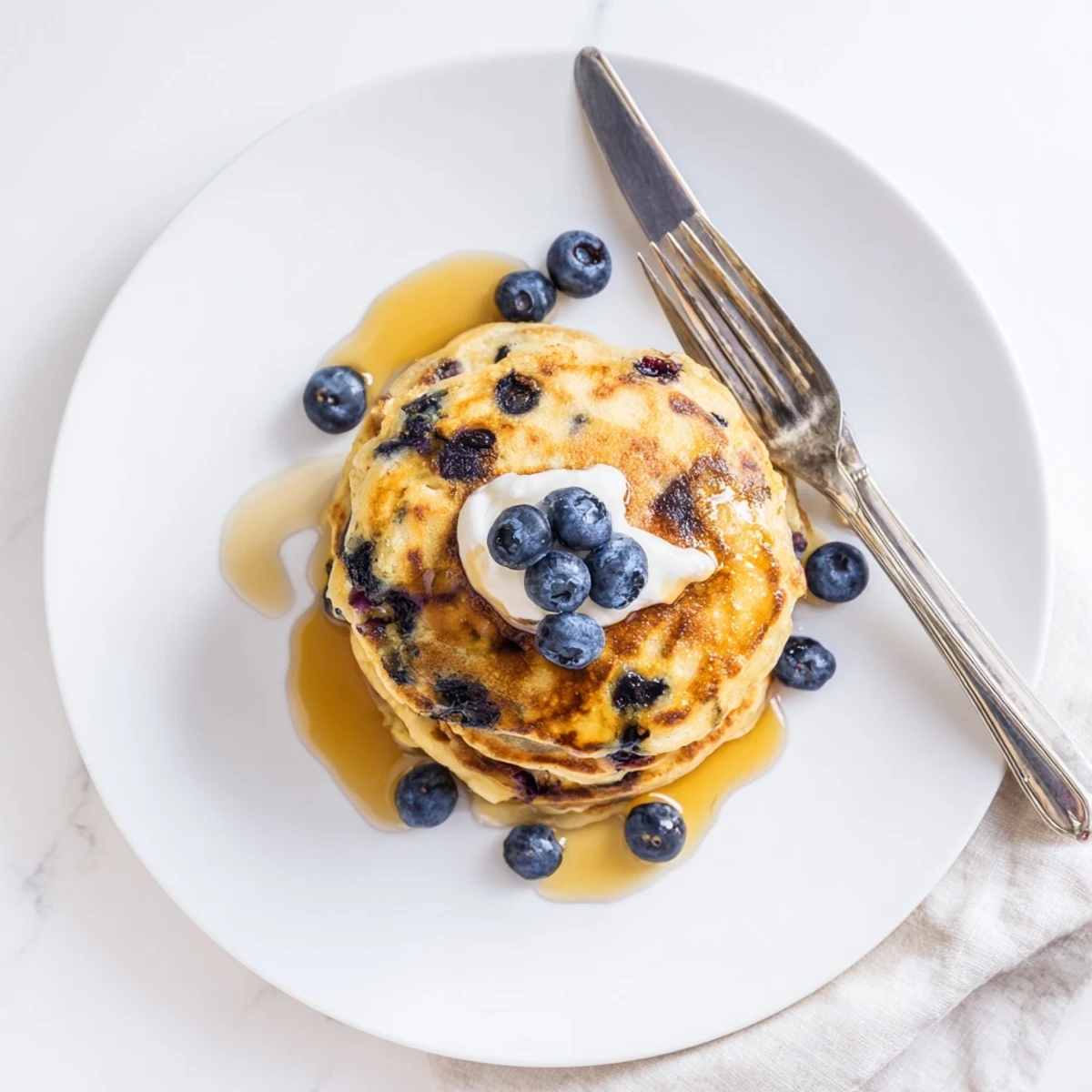 Close-up of Fluffy Greek Yogurt Blueberry Pancakes with creamy yogurt dollop and warm maple drizzle.