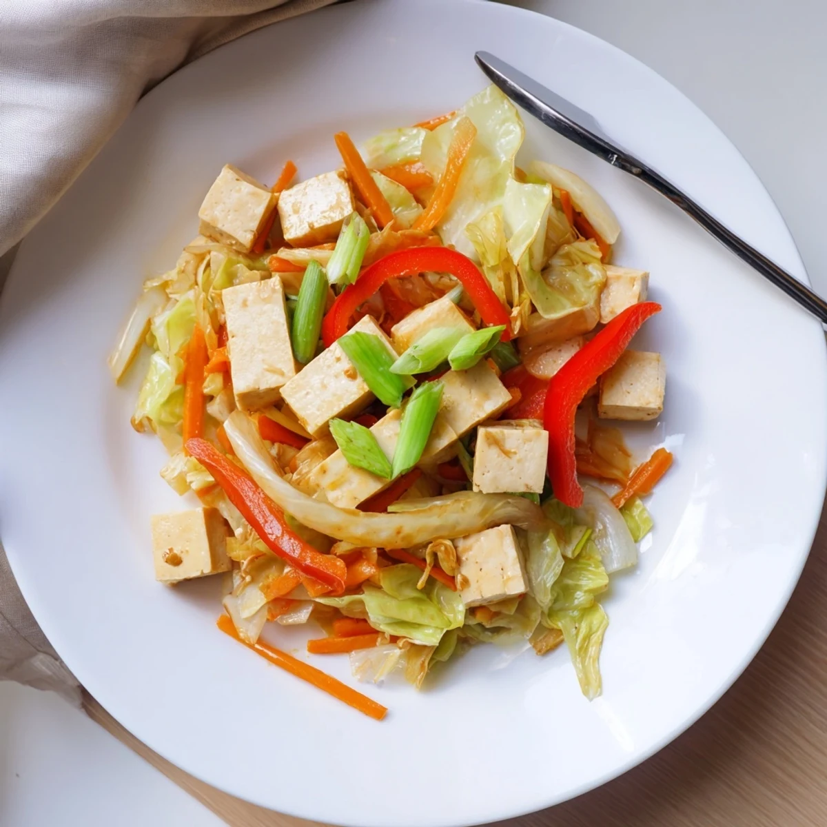 Golden-brown crispy tofu cubes mixed with bright green cabbage and red bell peppers in a savory garlic-ginger sauce, ready to serve.
