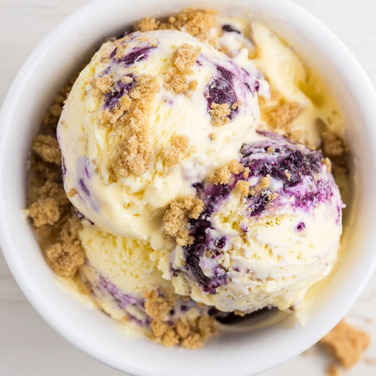 Fresh blueberries and lemon zest garnish this homemade Lemon Blueberry Cheesecake Ice Cream served on a sunny patio table.
