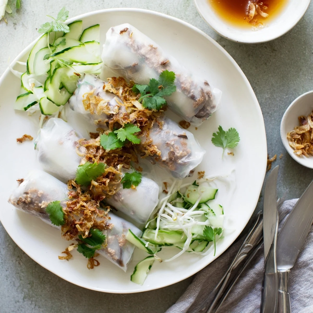 Steamed Banh Cuon rice rolls stuffed with savory pork and wood ear mushrooms, garnished with crispy shallots, fresh herbs, and cucumber slices.