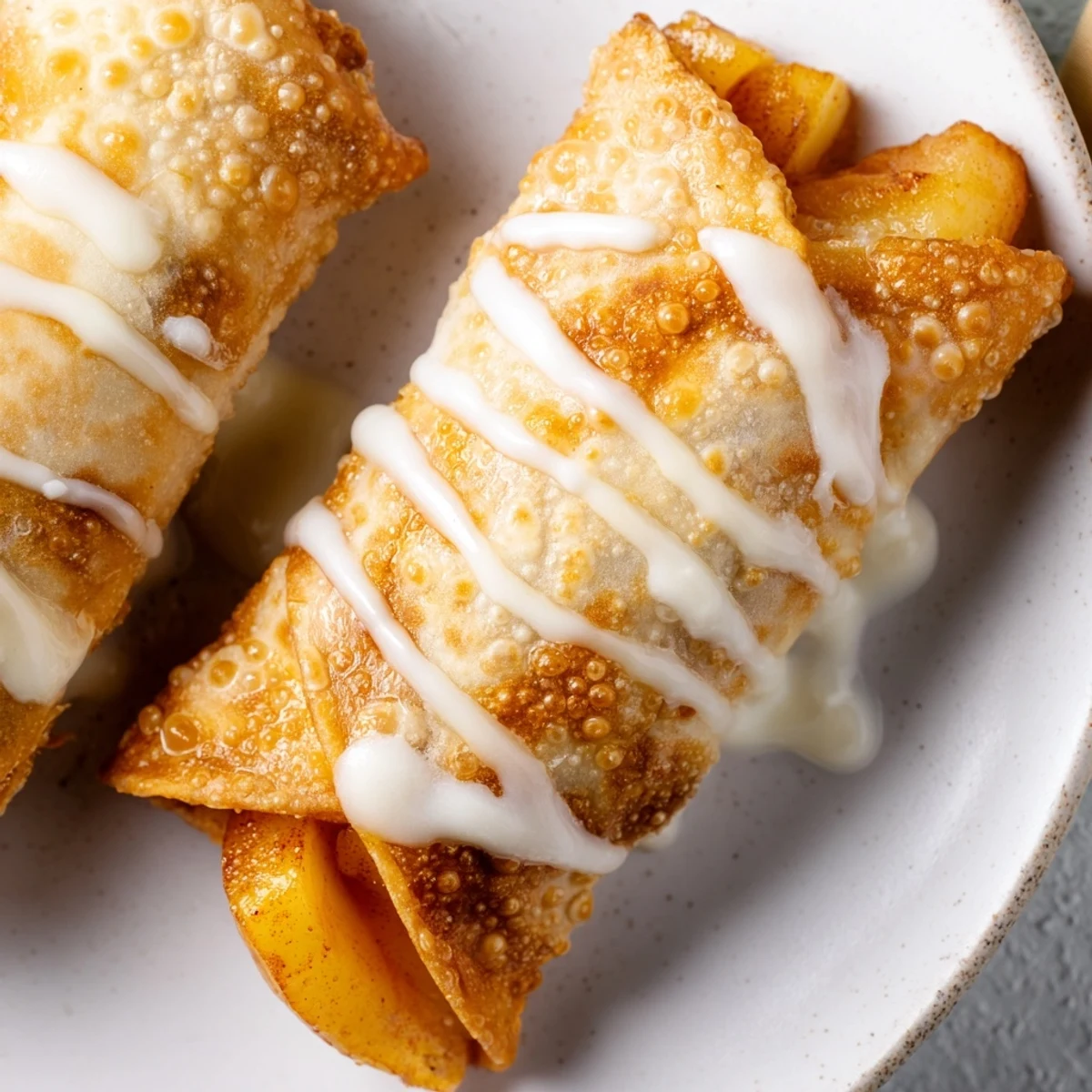Golden peach cobbler egg rolls drizzled with white vanilla glaze on white plate
