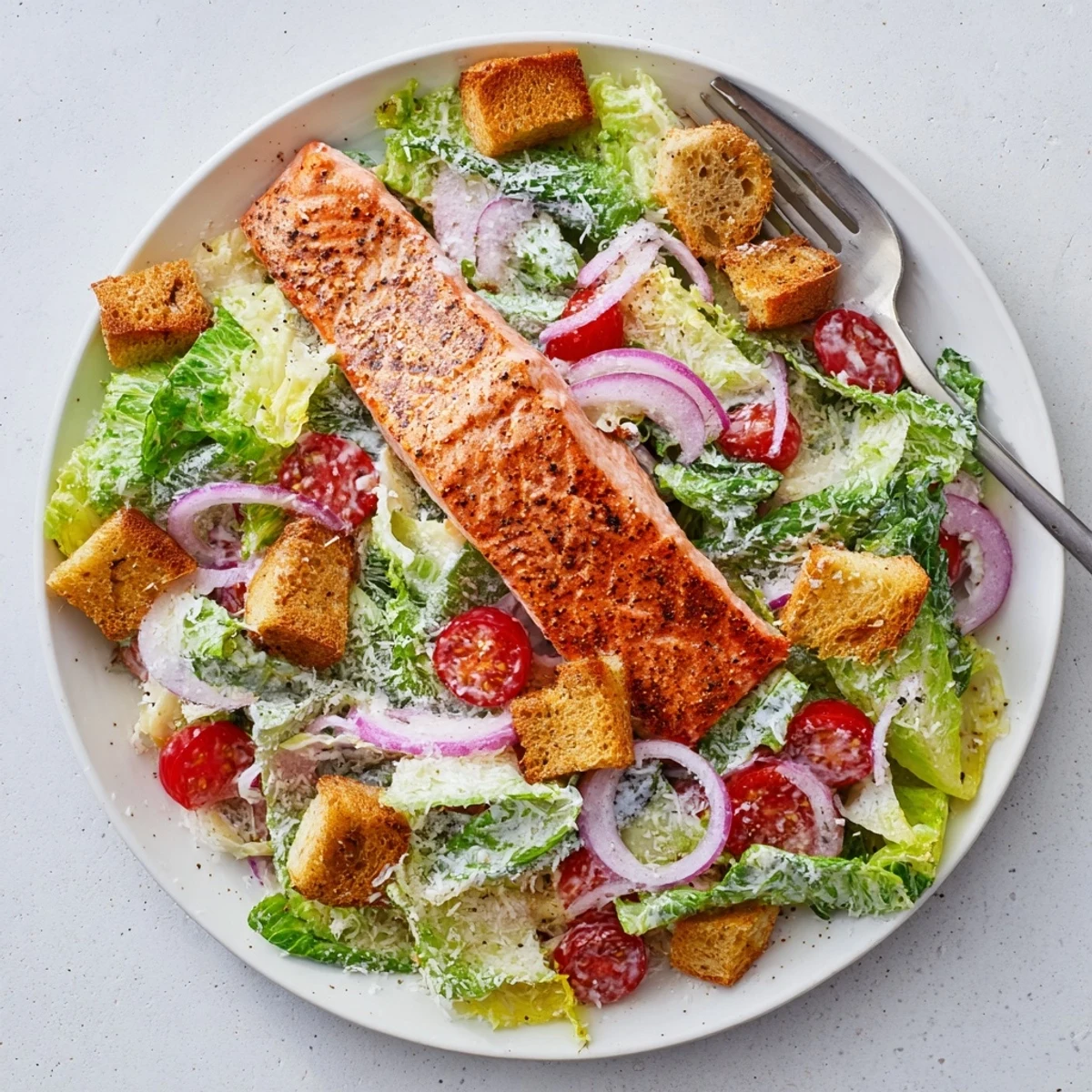 Flaky salmon Caesar salad featuring fresh cherry tomatoes red onion and creamy homemade dressing on white plate