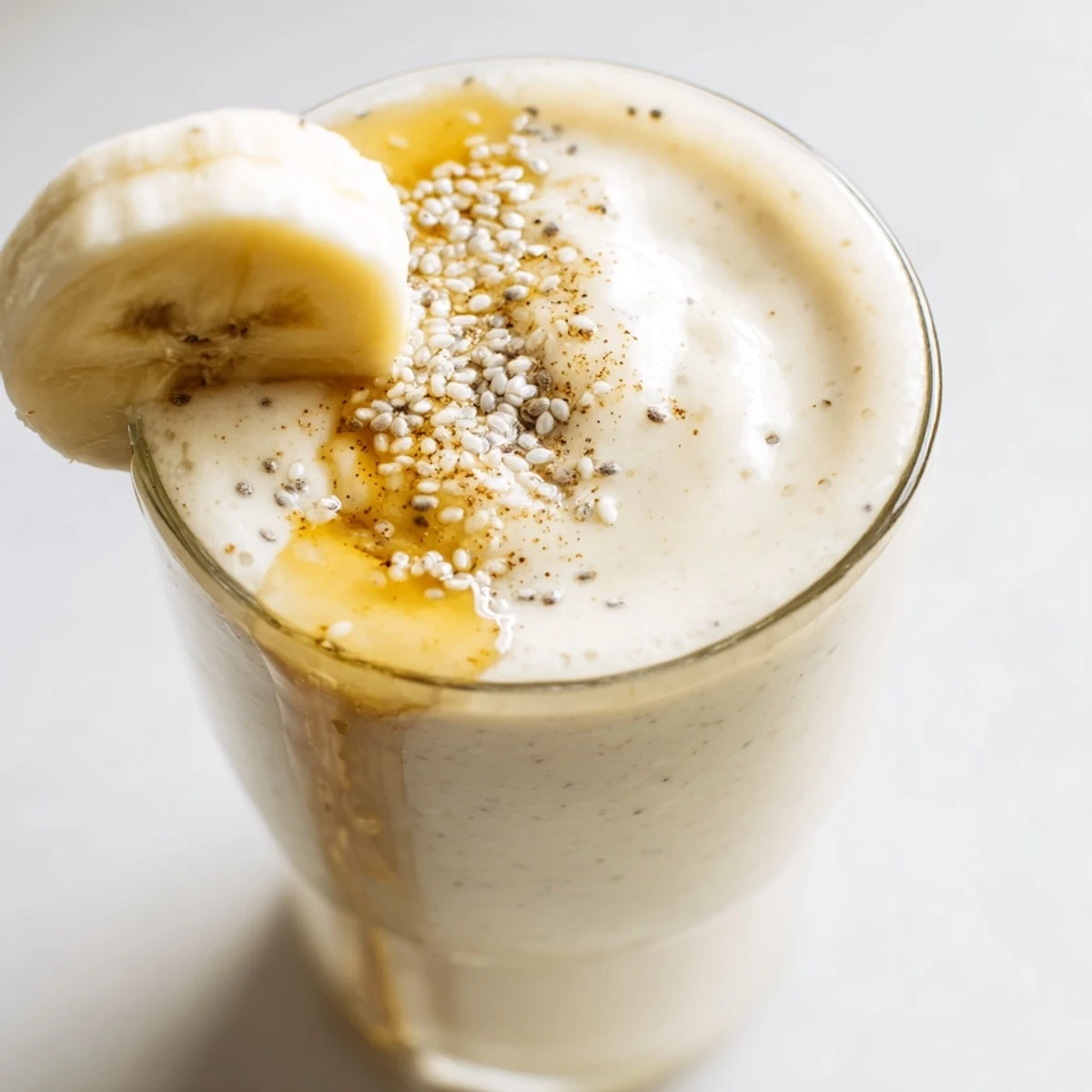 Homemade Greek yogurt banana smoothie poured into two glasses with ice and honey drizzle