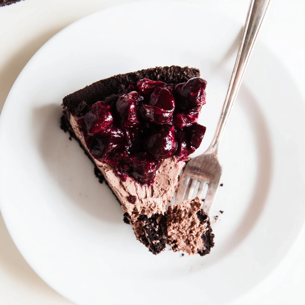 Creamy dark chocolate cherry cheesecake slice with glossy red cherry topping drizzled over chocolate crust