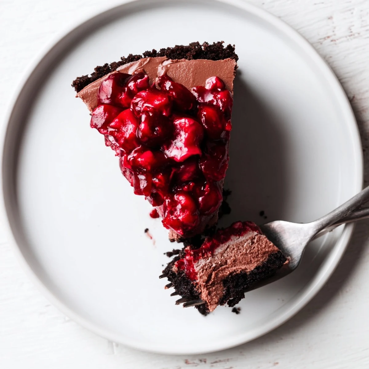 Rich dark chocolate cherry cheesecake wedge showcasing smooth chocolate layers and fresh ruby cherry compote
