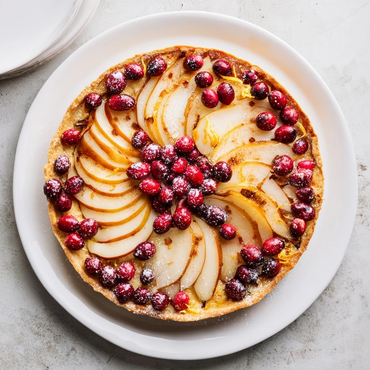Festive holiday dessert showcasing spiced pears and vibrant red cranberries in a golden tart pan