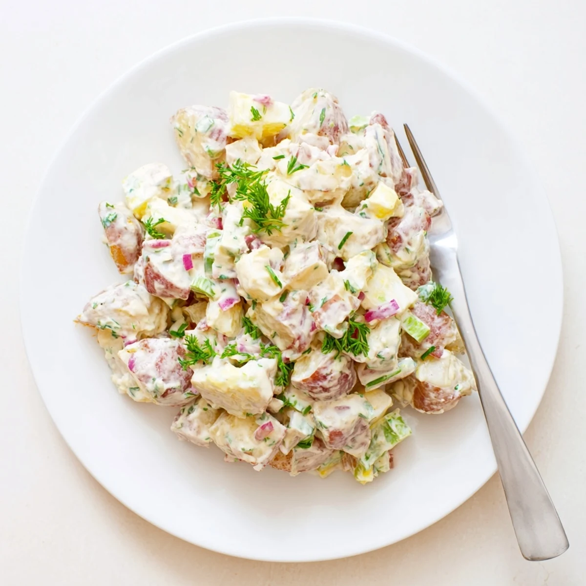 Vibrant red potato salad featuring creamy dressing, red onion, and parsley on a white serving plate