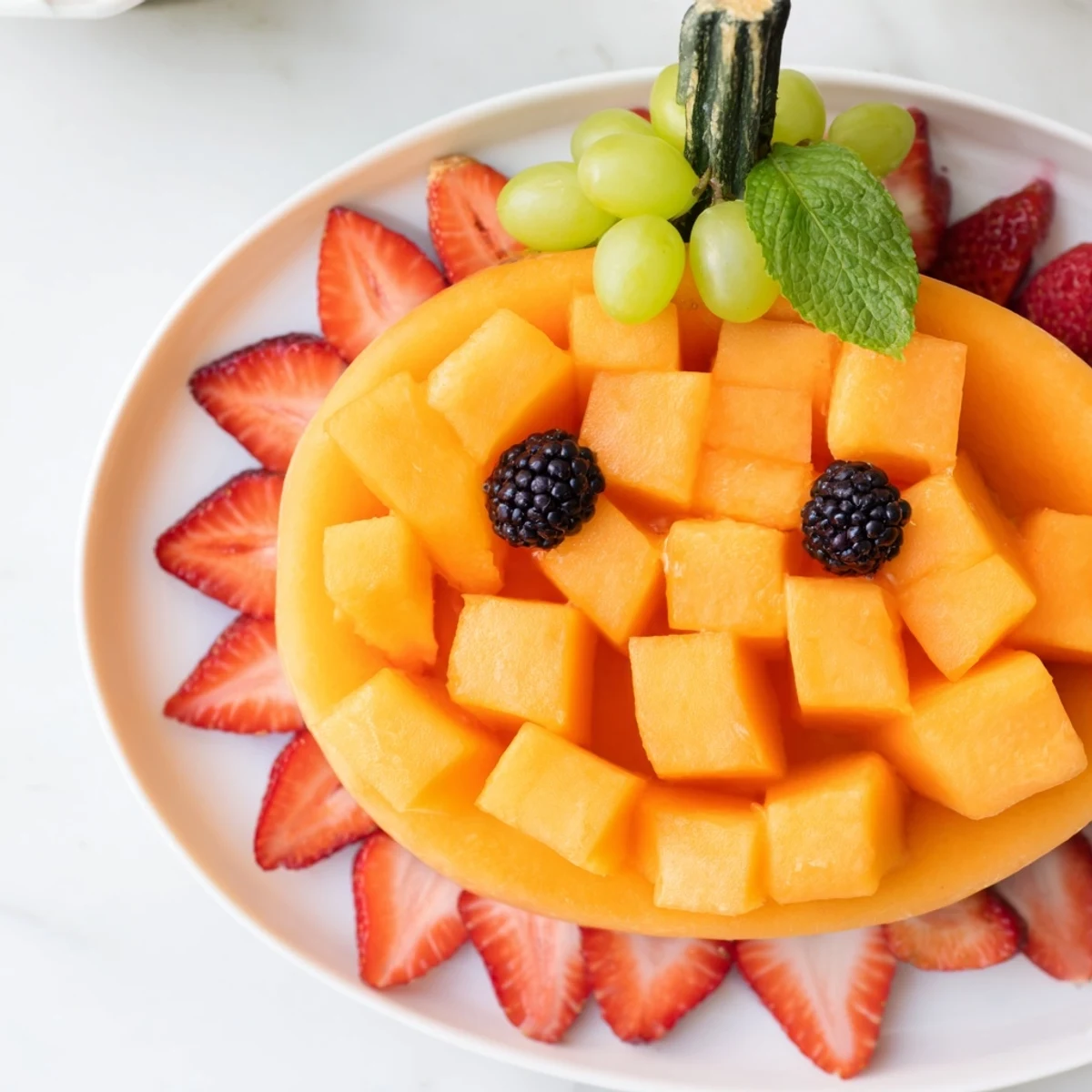 Healthy pumpkin fruit tray Halloween platter displaying vibrant orange cantaloupe decorated with dark berries for a fun party appetizer