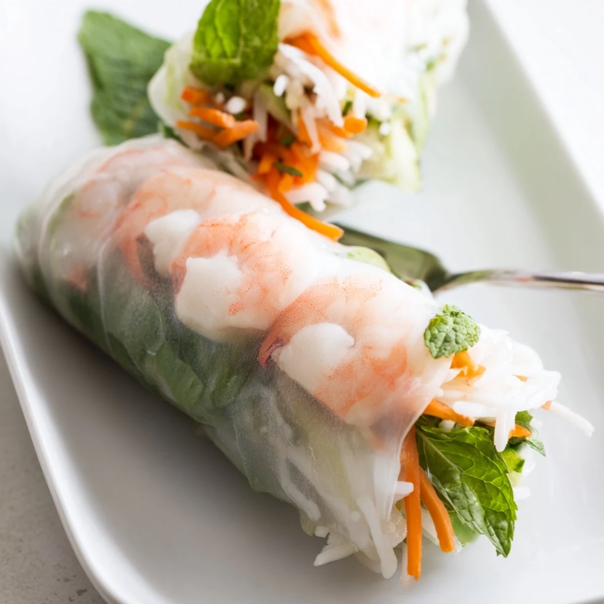 Close-up of translucent spring rolls filled with shrimp and colorful vegetables beside creamy peanut dipping sauce