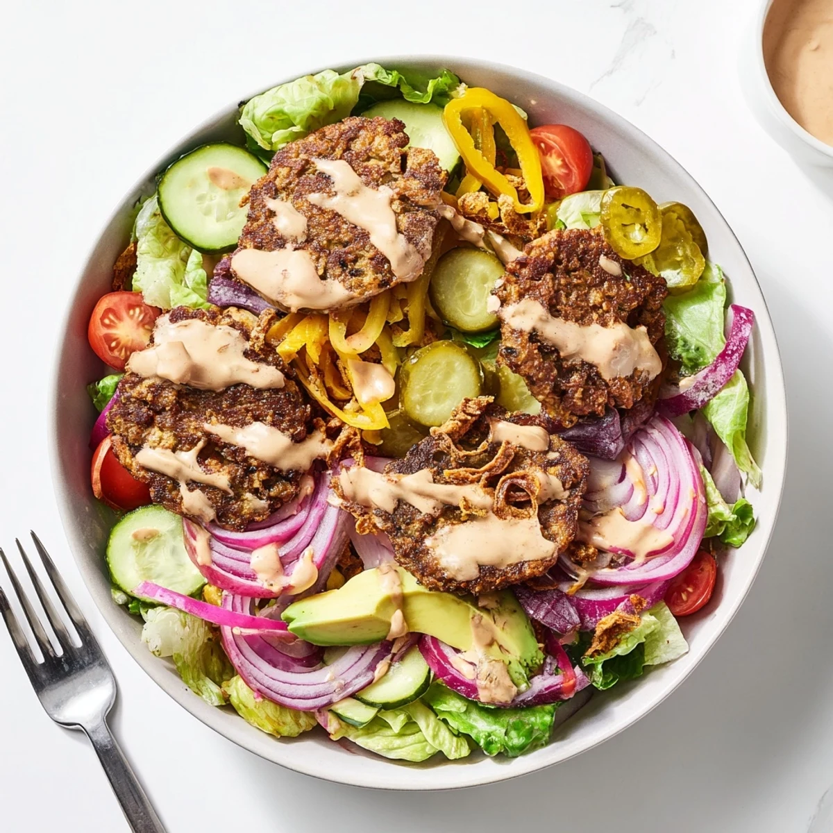 Golden crispy smash burger patties nestled over fresh greens with juicy tomatoes and tangy pickles in a healthy Smash Burger Bowl