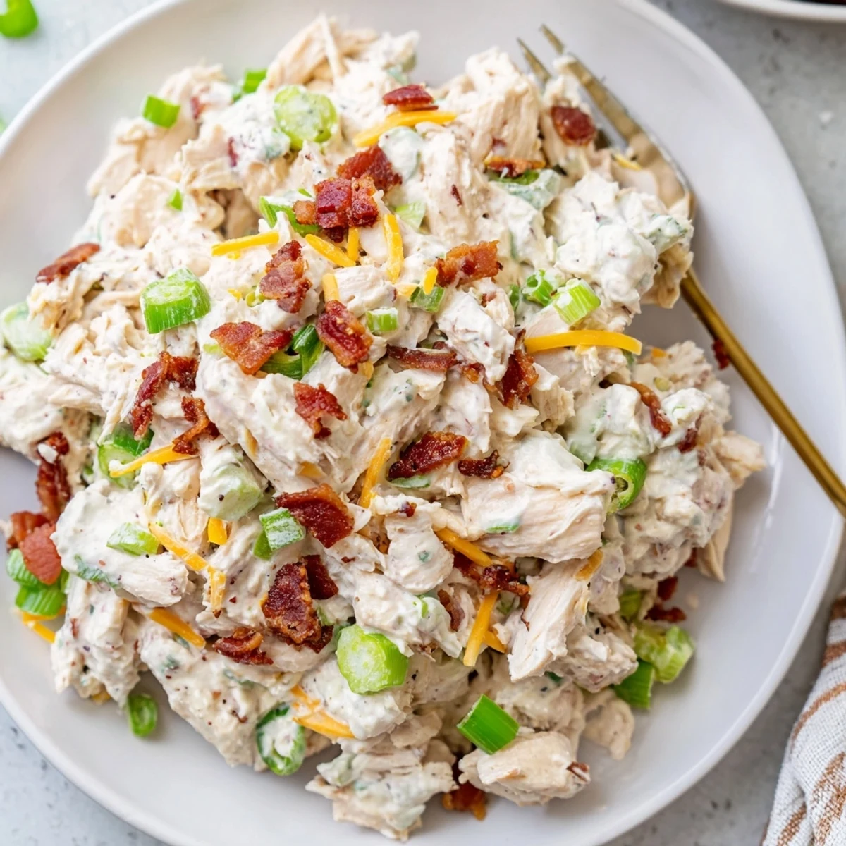 Creamy jalapeno popper keto chicken salad served in a white bowl with crispy bacon bits sprinkled on top and fresh green onions