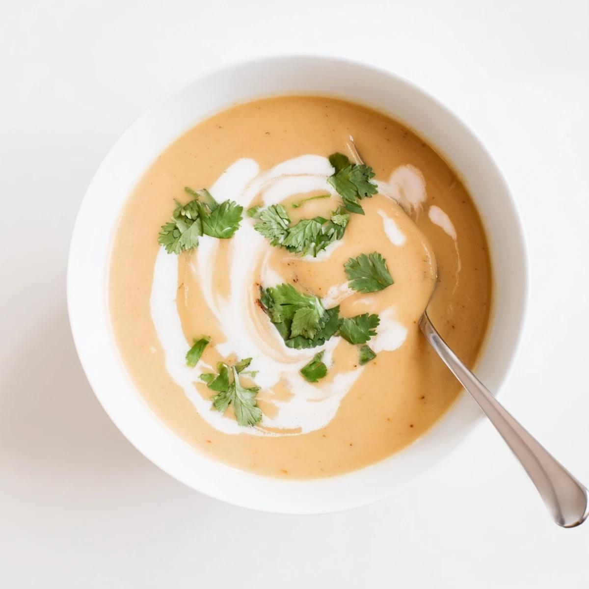 Creamy spicy apple soup recipe garnished with fresh herbs and coconut swirl in rustic bowl