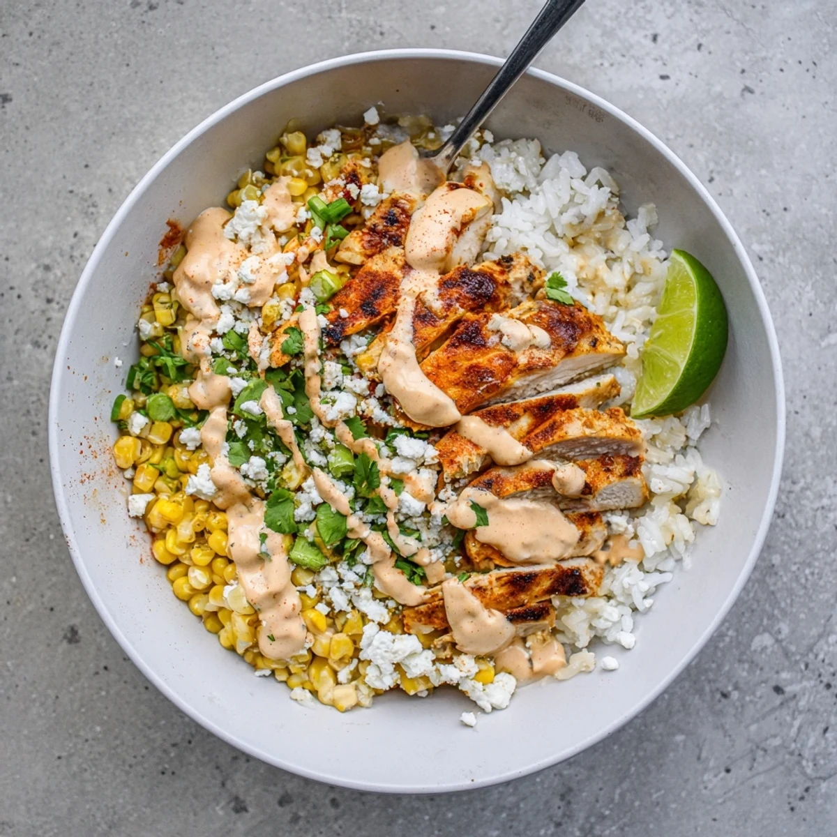 Sliced grilled chicken atop charred corn and fluffy rice in a street corn chicken rice bowl.