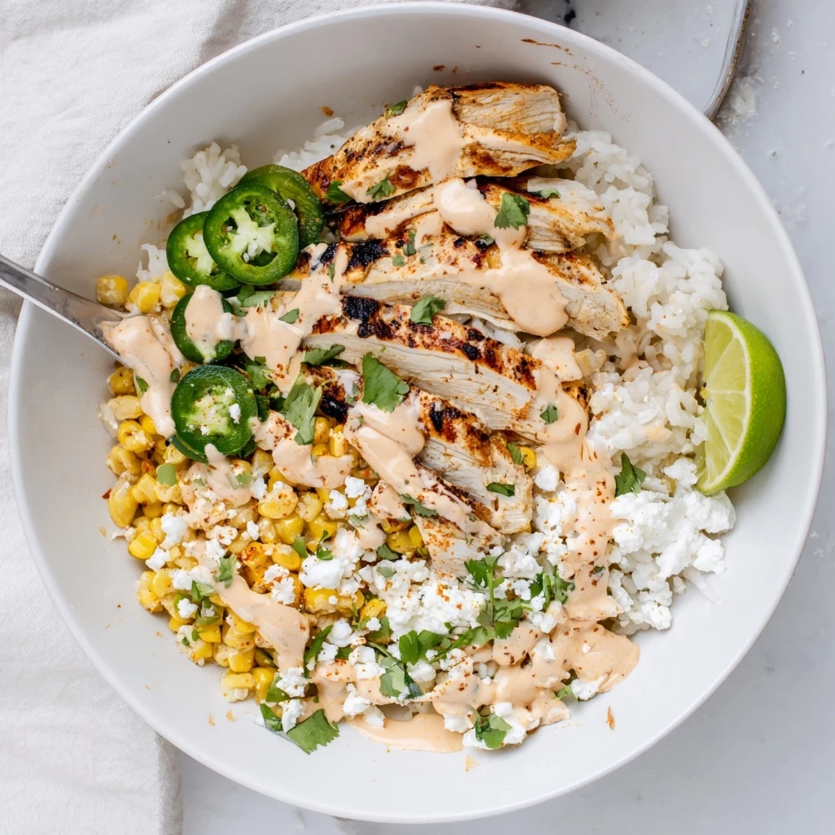 Steaming street corn chicken rice bowl garnished with fresh cilantro, jalapeño, and lime wedges.