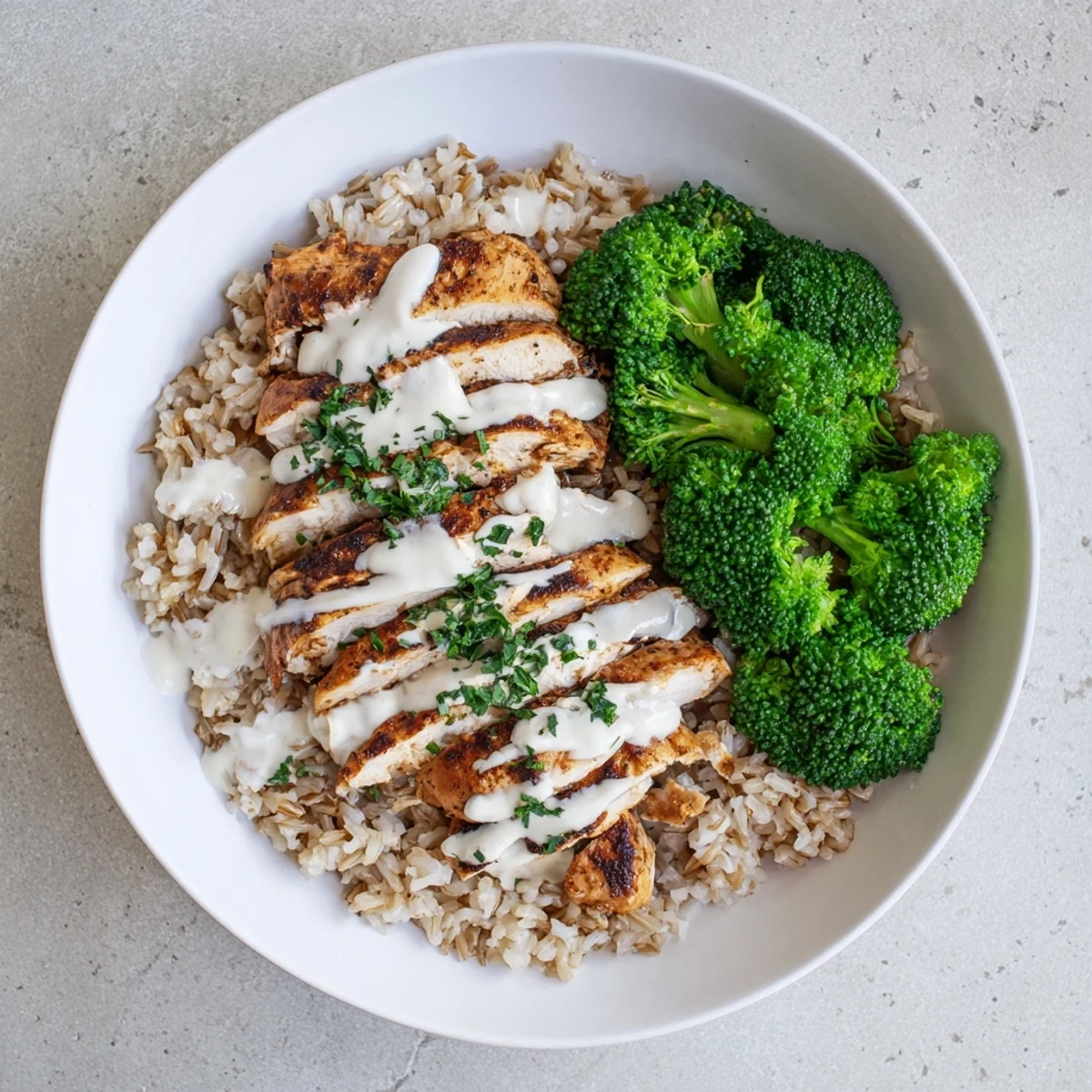 Golden grilled chicken slices and bright green broccoli florets drizzled with creamy garlic sauce in a healthy bowl