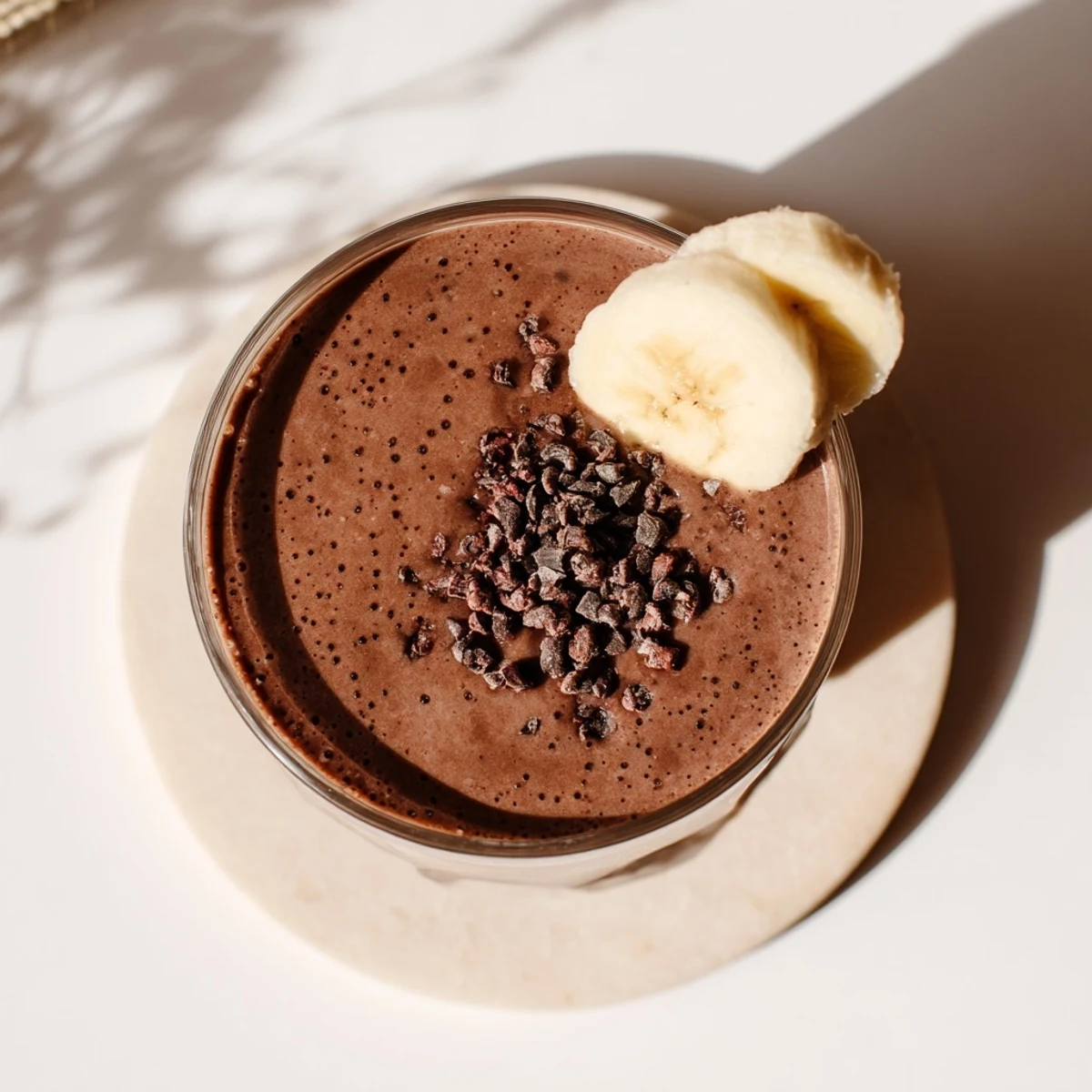 Creamy raw chocolate banana shake poured into tall glasses with banana slice garnish