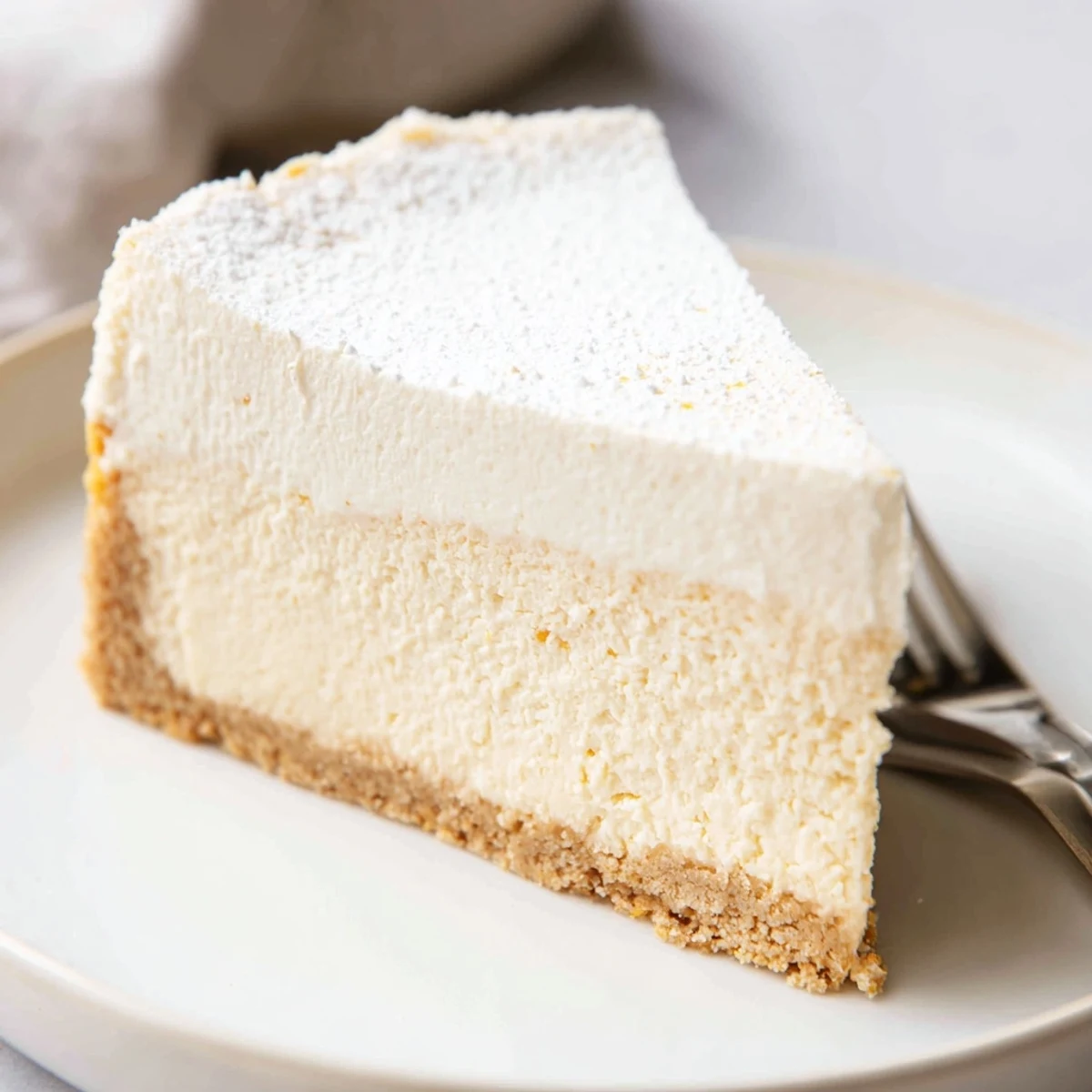 Tall, velvety cheesecake slice revealing a buttery cookie crust and rich filling
