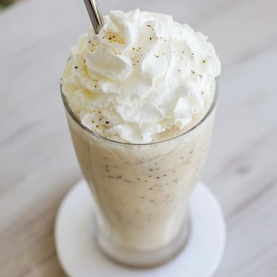 Vanilla Bean Frappuccino in a frosty glass with a straw, creamy texture and ice crystals visible.  