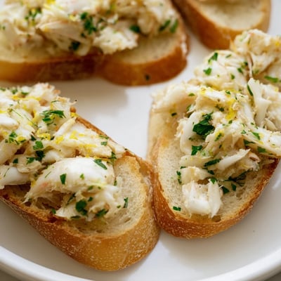 Golden garlic butter crab toasts glistening with lemon and herbs on a serving platter.