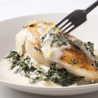 Savory lemon Parmesan spinach chicken plated with fresh herbs and a side of roasted vegetables.